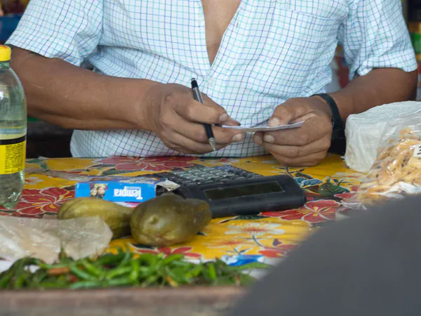 Manos de un vendedor anotando a mano sobre el mostrador de su puesto, junto a una calculadora